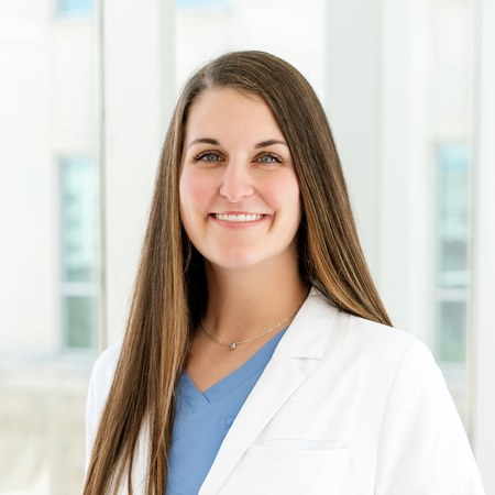 McKenna Steele, FNP-C, wearing a white coat over blue scrubs, smiling.