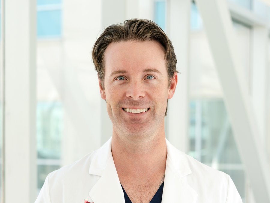 Dr. Kyle Norris, wearing a white coat over navy scrubs, smiling.
