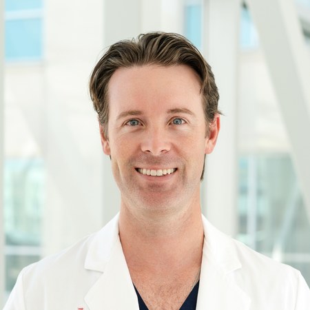 Dr. Kyle Norris, wearing a white coat over navy scrubs, smiling.