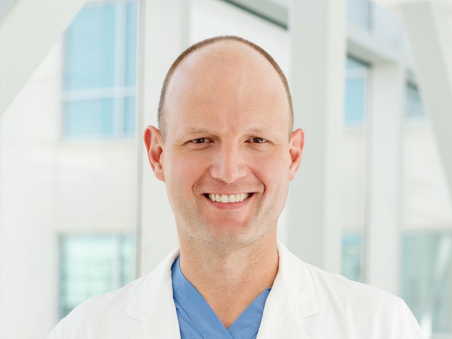 Dr. Christopher Ripperda, wearing a white coat over blue scrubs, smiling.