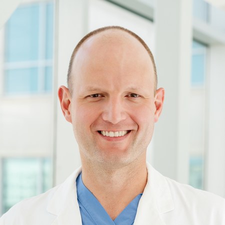 Dr. Christopher Ripperda, wearing a white coat over blue scrubs, smiling.